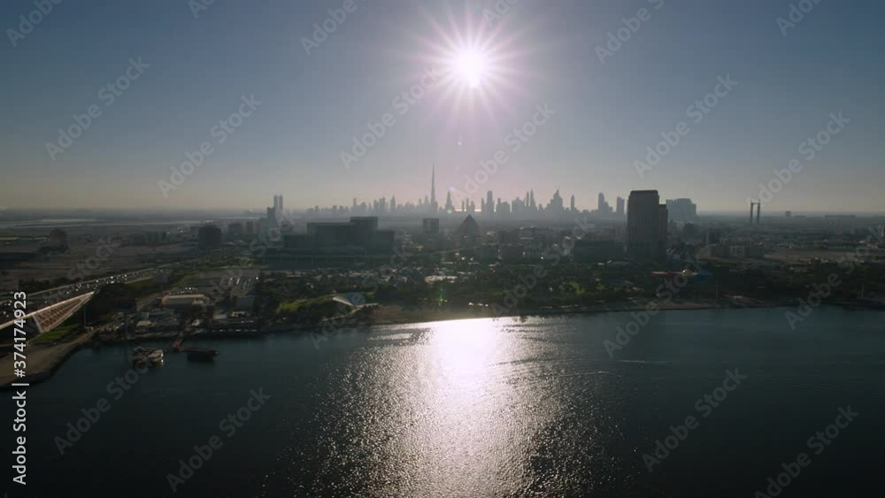 Tilting down to a panoramic view over the Dubai Creek passing Al Garhoud bridge with the sun above the Burj Khalifa and the Dubai Skyline, Aerial, 6-axis stabilized gimbal, Shotover F1, 8K, parallax. Tilting down to a panoramic view over the Dubai Creek passing Al Garhoud bridge with the sun above the Burj Khalifa and the Dubai Skyline, Aerial, 6-axis stabilized gimbal, Shotover F1, 8K, parallax.