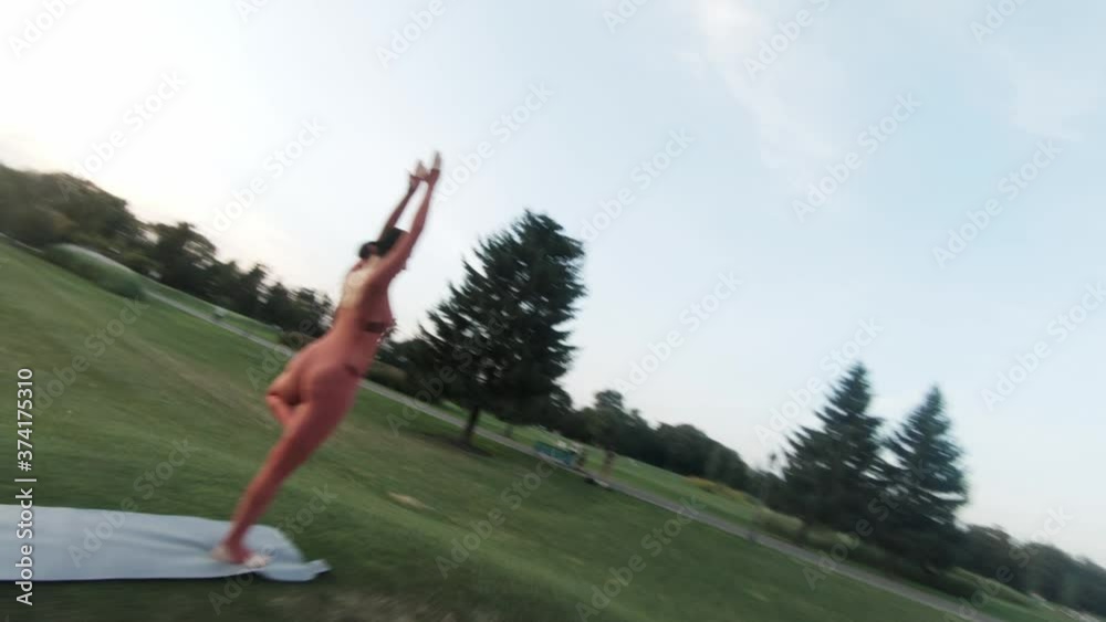 Creative aerial shot with fpv racing drone of woman in red tracksuit doing yoga in the park at sunny day at sunset.