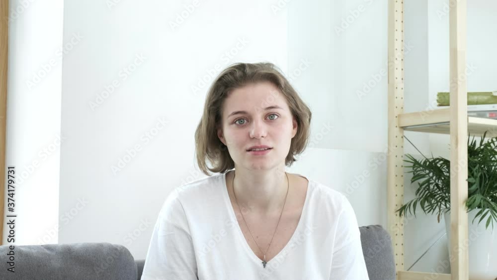young woman sitting on sofa at home gets shocking news, gets upset, cannot believe, feels stress, hopelessness, tries to restrain herself, cries. depression, sorrow, grief, misery, desperation, shock young woman sitting on sofa at home gets shocking news, gets upset, cannot believe, feels stress, hopelessness, tries to restrain herself, cries. depression, sorrow, grief, misery, desperation, shock