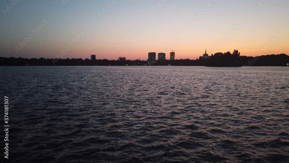 Waves on Herastrau Lake, Bucharest at sunset with distant buildings on background Waves on Herastrau Lake, Bucharest at sunset with distant buildings on background