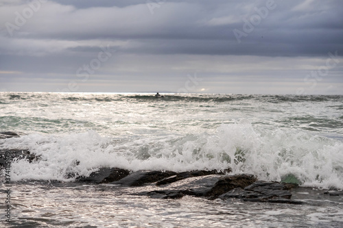 Powerful ocean waves and surfer in black wet suit, Cloudy sky.
