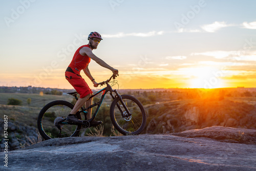 The cyclist rides on the rocks on a mountain bike, in the background of a sunset, a copy of the free space. © mihakonceptcorn