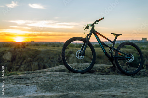 A full suspension mountain bike stands on a rock against the backdrop of a sunset. MTB. Cycling.