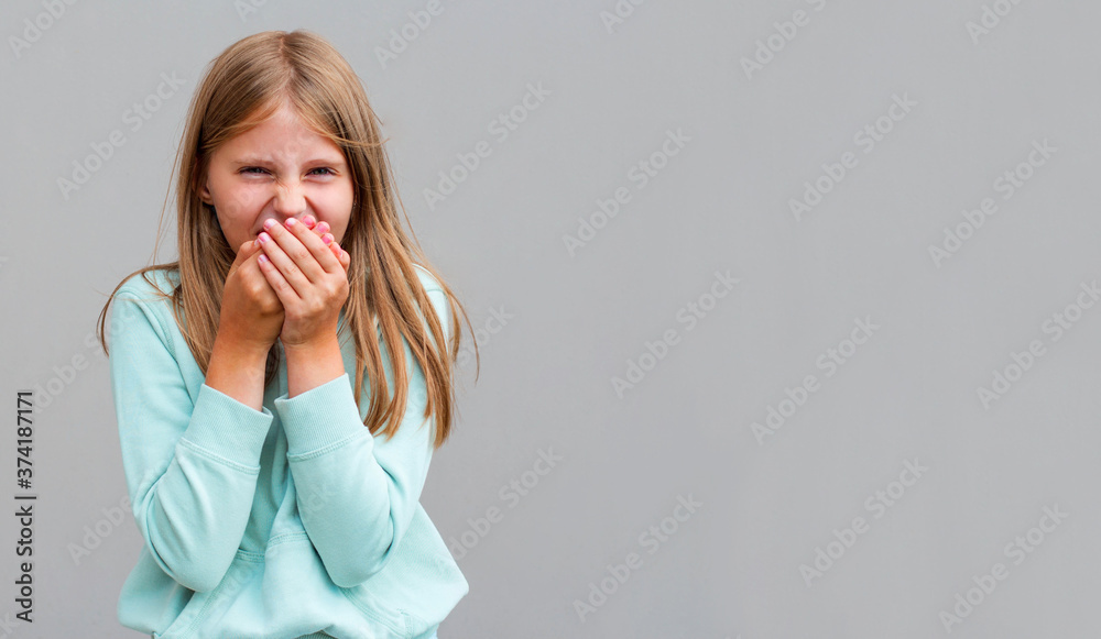 Happy preteen girl covering her mouth and laughing isolated on gray background Happy preteen girl covering her mouth and laughing isolated on gray background