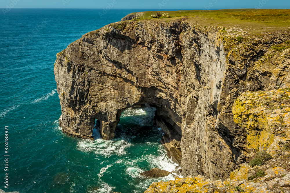 Fototapeta premium A view of an arch on the Pembrokeshire coastline seen from the Green Bridge of Wales in summer