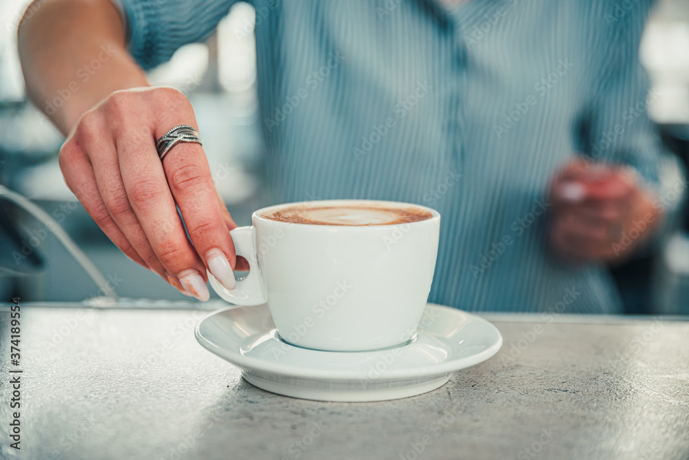 Closeup female barista hands holding cup of aromatic latte or cappuccino coffee in bar or cafe Closeup female barista hands holding cup of aromatic latte or cappuccino coffee in bar or cafe