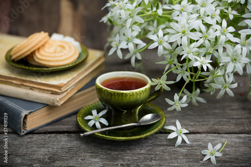 A cup of tea vintage on the background of a bouquet with white flowers, old books, cookies and an old wooden background