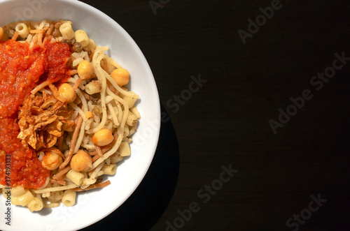 Famous traditional Arabic, Egyptian dish - Koshari. National Kushari in a white plate on dark wooden background with copy space. Flat lay, top view. photo