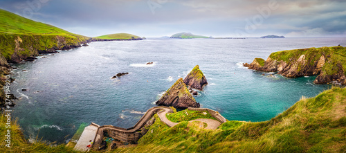 Beautiful view on Dunquin Harbour and small rocky islands with turquoise water and green fields in the background. Dingle peninsula, Co Kerry, Ireland