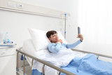 Happy child lying in bed alone in hospital room taking selfie with smartphone with copy space