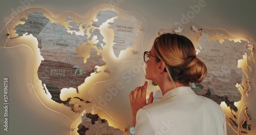 woman in white business suit looking at the world map on the wall in the room