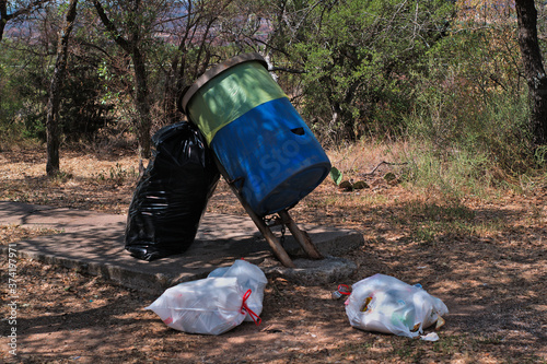 Trash spilling out top of barrel piled up bags around it dumped at a roadside rest stop causing pollution and enviromentally damaging ecosytem of habitat. photo