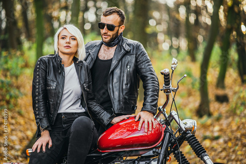 Pretty couple near red motorcycle on the road in the forest with colorful blured background