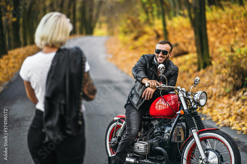 Pretty couple near red motorcycle on the road in the forest with colorful blured background