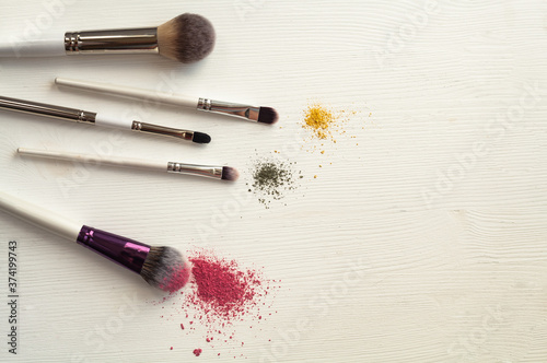 Makeup brushes with blusher and eyeshadow sample on white background