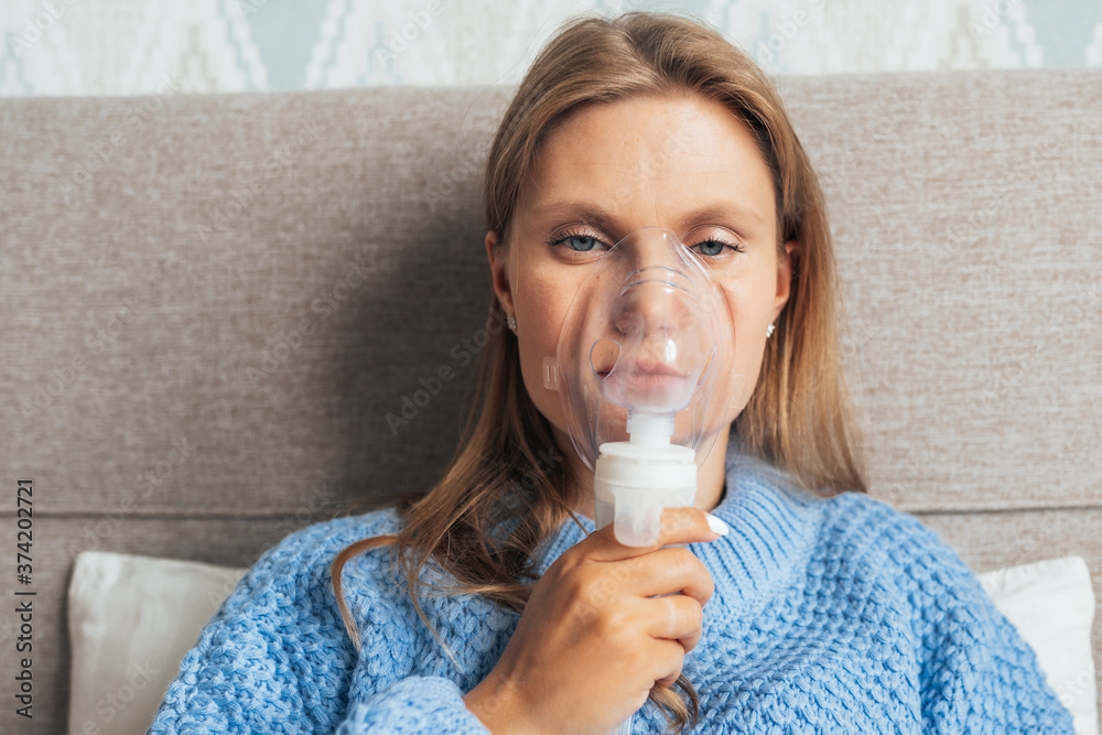 Portrait of a young blonde woman doing inhalation with steam nebulizer at home. Asthma, flu, health care concept. Portrait of a young blonde woman doing inhalation with steam nebulizer at home. Asthma, flu, health care concept.