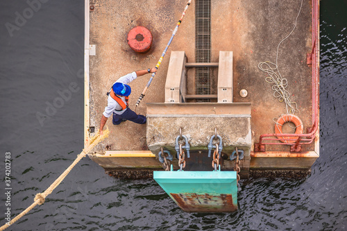 Dockworker wearing a life jacket using a boat hook to grab the hemp mooring line of the Kanayamaru ferry and hang it on a bollard of the pier of Kurihama port. photo