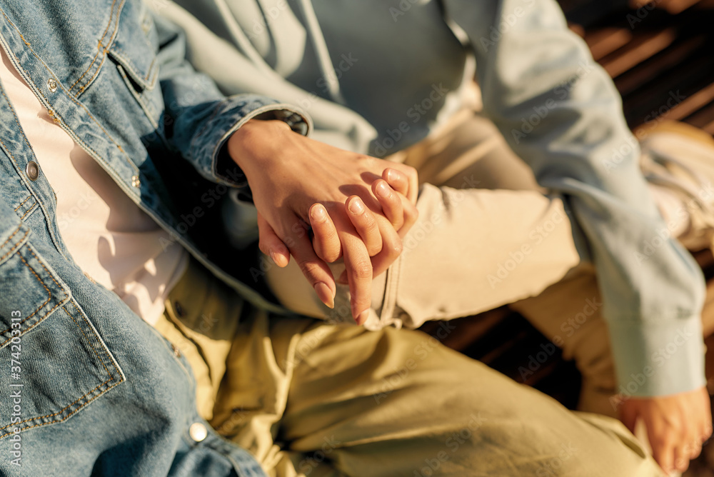 Close up of hands of lesbian couple. Two girls holding their hands, sitting on the bench on a sunny day while spending time together outdoors