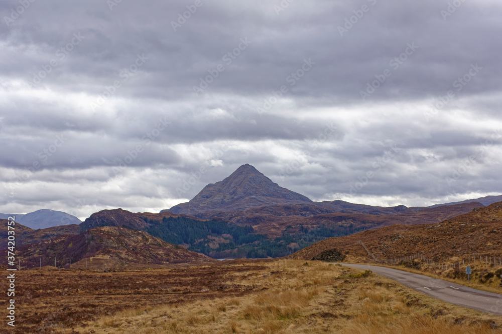 Dramatic Mountain Scenery on the road through the North West Highland Global Geopark in Assynt, with a triangular peak in the background. Dramatic Mountain Scenery on the road through the North West Highland Global Geopark in Assynt, with a triangular peak in the background.