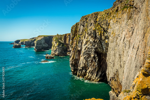 The view along the Pembrokeshire coast, Wales showing the entrance to a Geo (collapsed cave with only entrance remaining), rock stacks and cliff faces in summer