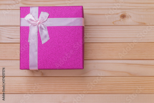a small bright sparkling purple holiday gift box with a pink lace bow on top lying on a wooden background, christmas gift-giving concept, complete little square container for birthday gifts