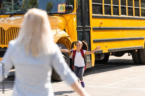 Kids student running into mother's hands to hug her after back to school near the school bus