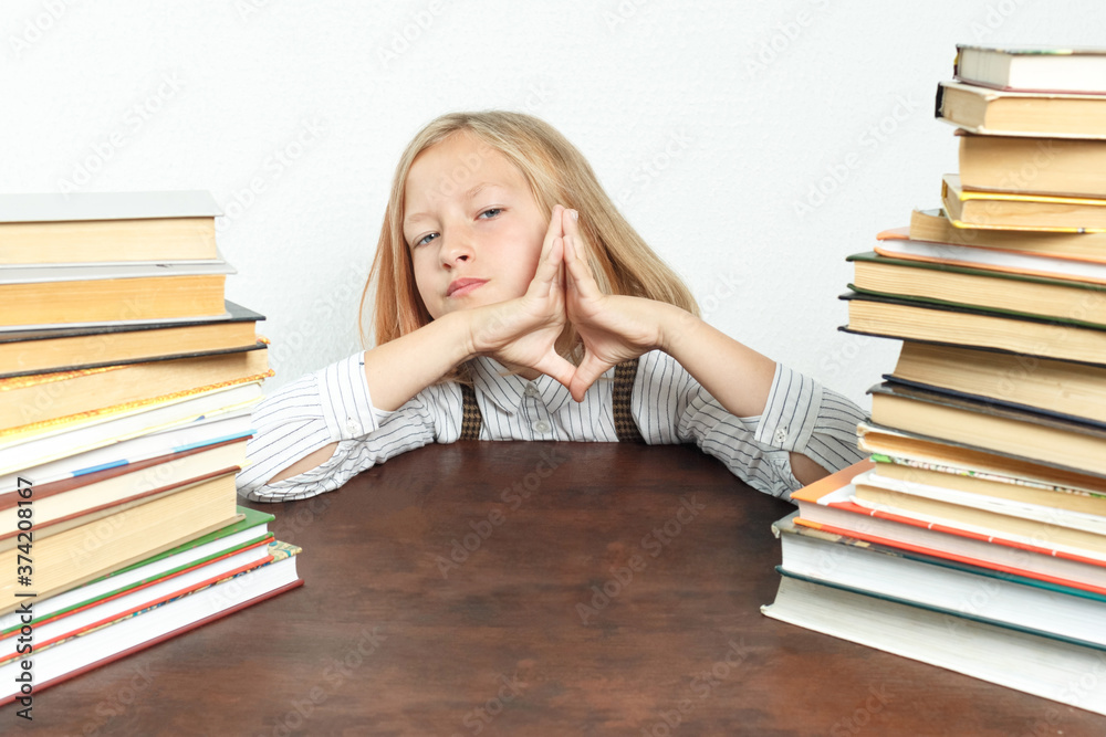 Portrait of a teenage girl who sits at a table tired among the books, her palms folded in front of her face. Portrait of a teenage girl who sits at a table tired among the books, her palms folded in front of her face.
