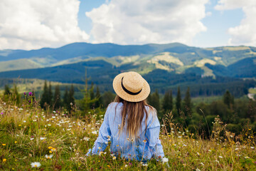 Traveling in summer Ukraine. Trip to Carpathian mountains. Woman tourist relaxing in flowers admiring view