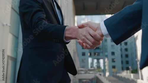 Close-up of two businessmen shake hands when meeting, agree to a deal or say hello. Handshake of two successful businessmen making a deal. Office building on background. Business district.