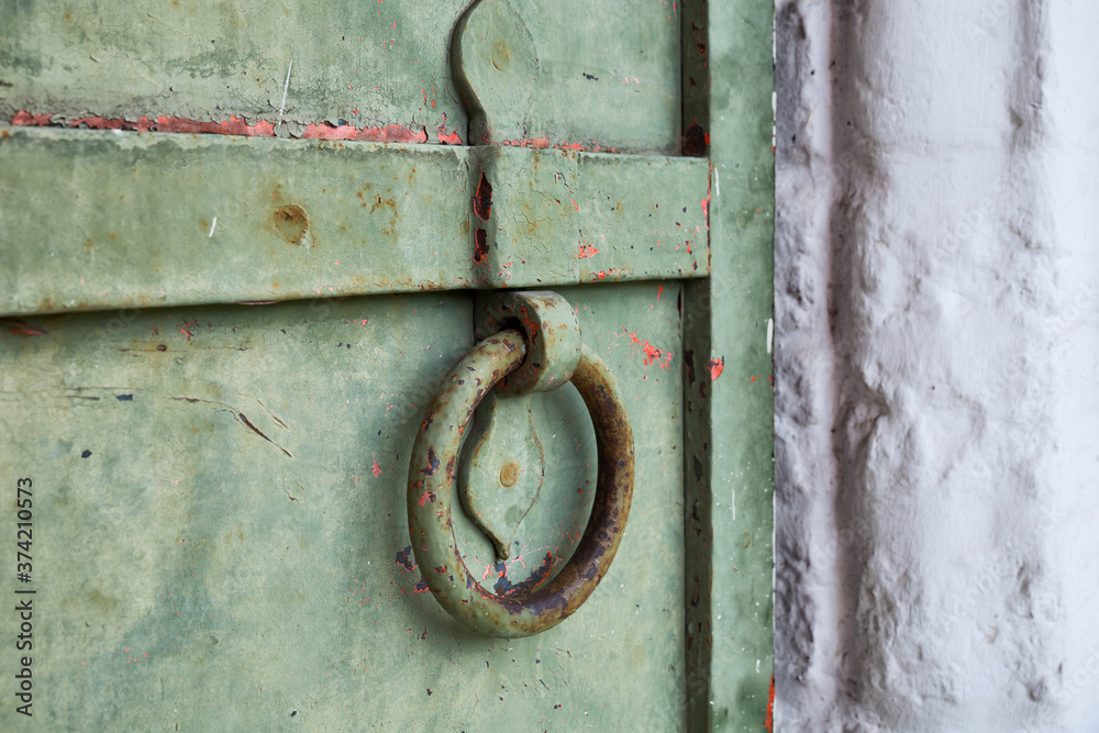 The old door with peeling paint and a ring-shaped handle. Vintage, old, toned image. Selective focus
