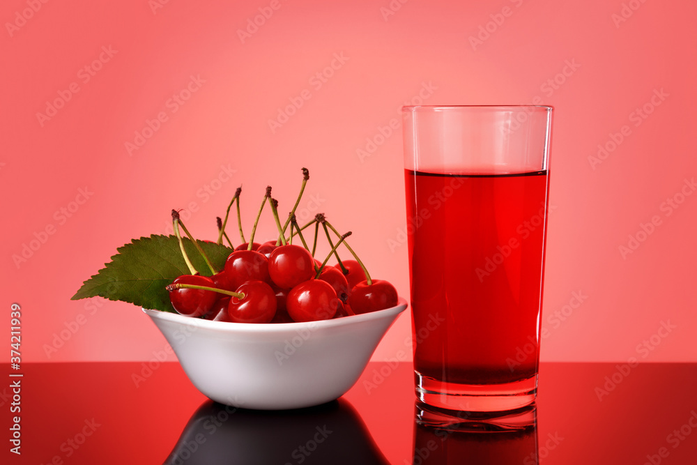 Glass of fresh cherry juice and some fresh cherries in bowl against bright red background. Glass of fresh cherry juice and some fresh cherries in bowl against bright red background.