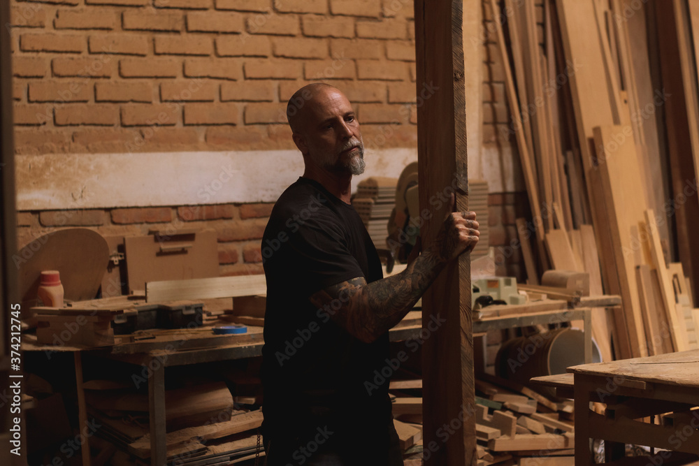 Fototapeta premium Hombre maduro mexicano trabajando carpintero en taller con madera tabla sierra martillo 