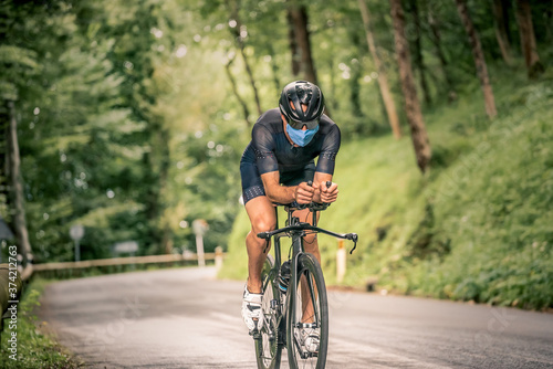 Fototapeta Naklejka Na Ścianę i Meble -  Man participating in triathlon with bicycle in mountain area with mask against the virus