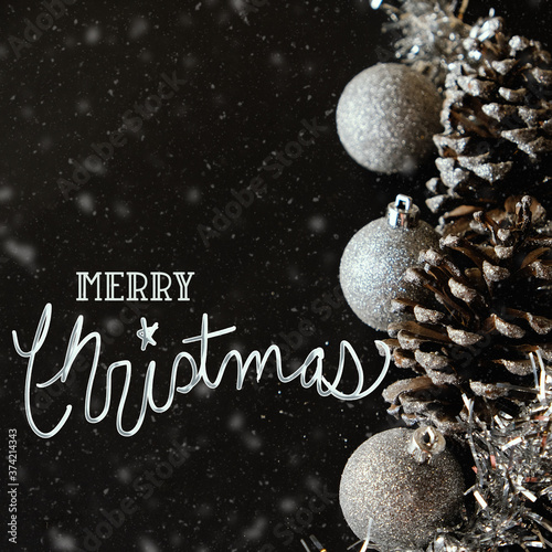 Christmas holiday decoration with silver ornaments and pine cones against black background.  Text for greeting or celebration. photo