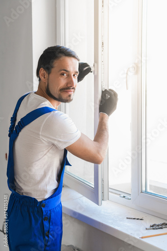 Male construction worker in overalls installs a window and poses at the camera