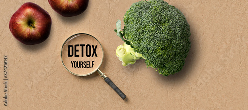 a magnifying glass with message DETOX and broccoli and apple on paper background photo