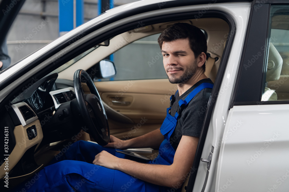 Car service worker in overalls sitting in a car in the front seat and looking at the camera Car service worker in overalls sitting in a car in the front seat and looking at the camera