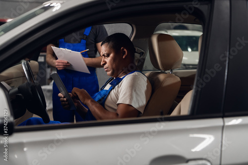 Two men inspect the car inside and use the tablet