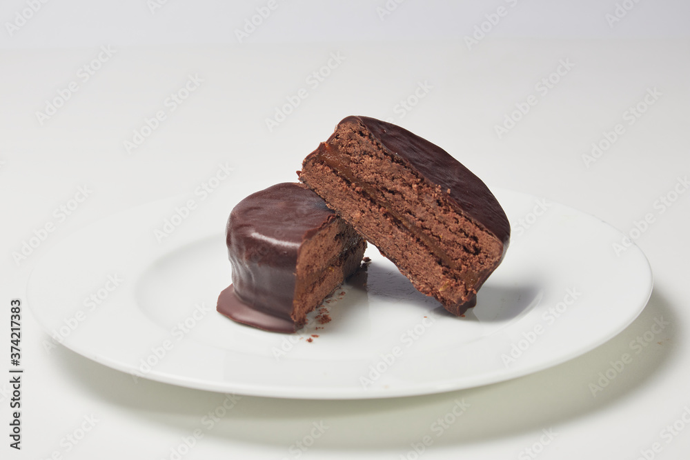 Typical Argentine Alfajor of dark chocolate cut in the middle where you can see the interior of chocolate and the filling of dulce de leche on a plate.