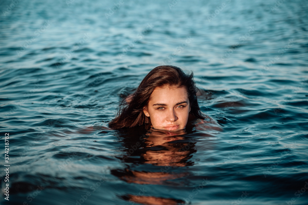 Beautiful young woman swiming in sea at sunset.
