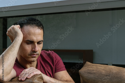Mature Brazilian man (44 years old) sitting on the brown sofa, behind the glass, sad and crestfallen. photo