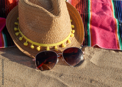 hat and sunglasses on the beach A hat  a beach coverlet and sunglasses lie on the sand of the sea shore  close-up side view.