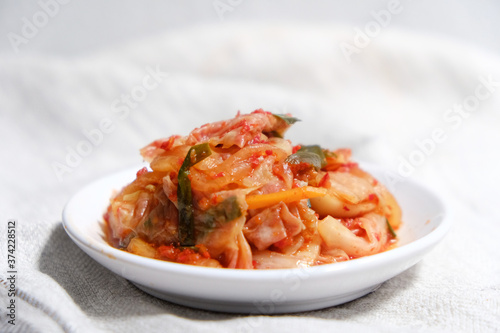 Kimchi is placed in a white plate with a fork on its side.