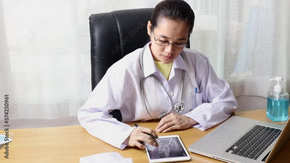 4K Women doctor looking x-ray on tablet and typing repoet of patient in to laptor. Doctor working in office clinic.. 4K Women doctor looking x-ray on tablet and typing repoet of patient in to laptor. Doctor working in office clinic..