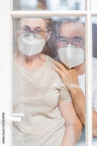Elderly couple wearing protective face masks watch through their home door during the coronavirus epidemic