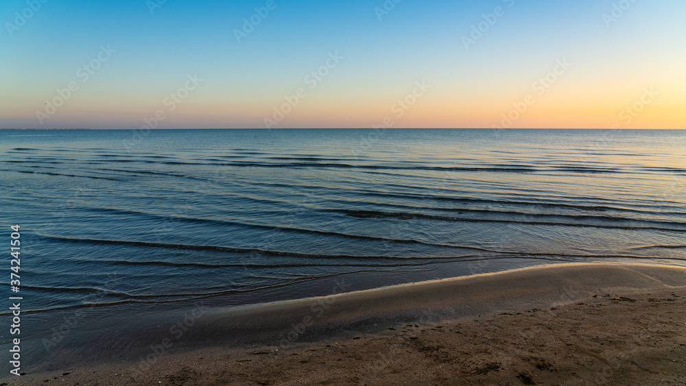 Sandy seashore with small waves before sunrise