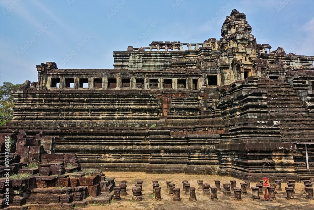 An ancient temple in the form of a stepped pyramid against the blue sky, decorated with carvings, ornaments. Galleries with columns, window openings. There is a staircase to the top. Cambodia. Angkor.