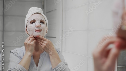 Adult woman with a towel on her head applying mask on her face and looking at the camera