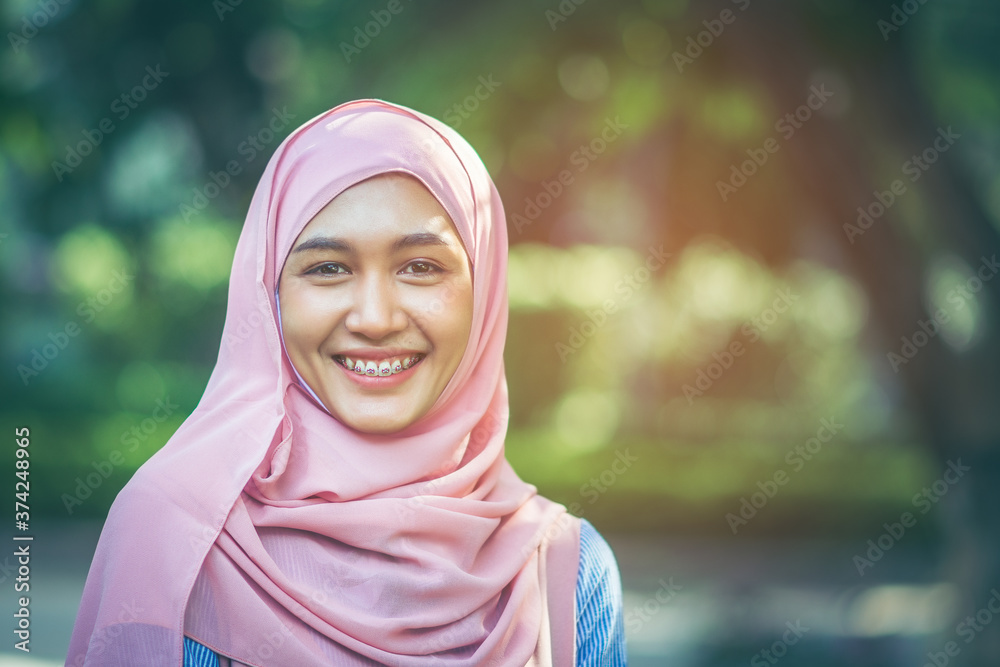 Beautiful Muslim Asian girl with a beautiful smile She wore braces and wore a pink hijab over her head, amid the lush atmosphere of the park with copy space. Beautiful Muslim Asian girl with a beautiful smile She wore braces and wore a pink hijab over her head, amid the lush atmosphere of the park with copy space.