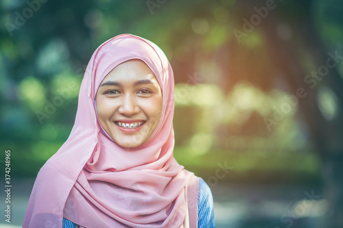 Beautiful Muslim Asian girl with a beautiful smile She wore braces and wore a pink hijab over her head, amid the lush atmosphere of the park with copy space.
